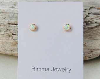 May include: A pair of small, round, white opal stud earrings with gold settings. The earrings are displayed on a white card with the text "Rimma Jewelry".
