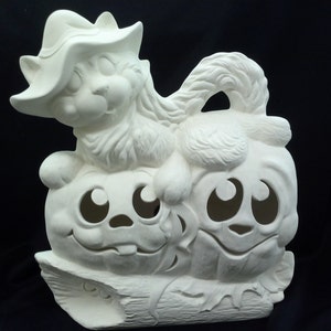 May include: White ceramic Halloween decoration featuring a cat wearing a hat sitting on top of two pumpkins. The pumpkins have carved faces with large eyes.