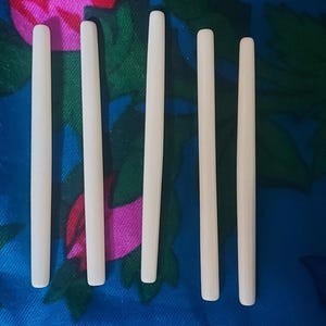 May include: Six off-white, cylindrical objects are arranged vertically against a floral patterned background. The objects appear to be made of a smooth material. The background features a mix of blue, pink, and green floral designs.