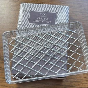 May include: A clear, rectangular crystal jewelry tray with a diamond pattern, and a matching box. The box has the text "AVON CRYSTAL JEWELRY TRAY" in a rectangular label. The tray is designed to hold jewelry.