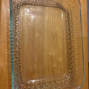 Puede incluir: Una fuente rectangular de vidrio transparente con un patrón de tejido de cesta texturizado en los lados exteriores. El fondo de la fuente es liso e incluye el texto en relieve Anchor Hocking, permitiendo ver claramente la superficie inferior.