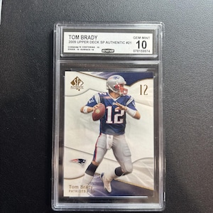 Puede incluir: Una tarjeta de fútbol de Tom Brady de la serie 2009 Upper Deck SP Authentic, calificada como GEM MINT 10. La tarjeta presenta a Brady con su uniforme de los Patriots, número 12. La tarjeta está dentro de un soporte protector.