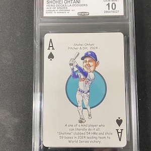 May include: A GEM MINT 10 Shohei Ohtani baseball card, Ace of Spades, featuring a cartoon illustration of the player in a Dodgers uniform. The card is encased in a protective holder with text that reads "Shohei Ohtani Pitcher & DH, 2024-".