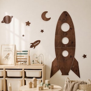 May include: A child's playroom with a wooden rocket-shaped growth chart, planets, stars, and a moon on the wall. The room includes a wooden table, chair, storage unit, toys, and a framed "Little Explorer" print.