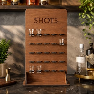 以下が含まれることがあります： 上部に「SHOTS」という文字が刻印された、木製の縦型ショットグラスディスプレイボード。ボードには5段の横列に円形の切り抜きがあり、それぞれに黒いリングが取り付けられており、小さな透明なショットグラスを保持できるようになっています。