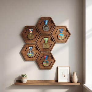 Puede incluir: Una exhibición montada en la pared de seis soportes hexagonales de madera para medallas, cada uno mostrando una medalla diferente. Los soportes están dispuestos en un patrón de panal. Una repisa de madera debajo sostiene una foto enmarcada, una pequeña planta en maceta y un jarrón.