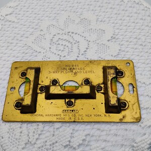 May include: A rectangular solid brass 3-way plumb and level tool, model No. 845, featuring three glass vials with yellow liquid. The metal surface is engraved with General Hardware Mfg. Co. Inc. New York, N.Y. Made in U.S.A. and secured with screws.