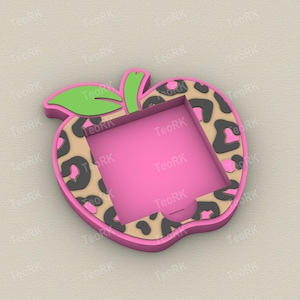 May include: A pink apple-shaped phone holder with a leopard print border. The holder has a bright pink interior and a green leaf and stem. The design is a fun and stylish accessory.