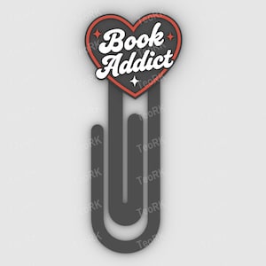 May include: A black bookmark with a heart-shaped top. The heart is outlined in red and features the words "Book Addict" in white. The bookmark has a unique, curved design.