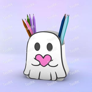 May include: A white ghost-shaped pencil holder with black eyes and a pink heart-shaped mouth. The holder contains several colored pencils in shades of brown, pink, purple, blue, and teal. The design is whimsical and playful.