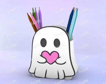May include: A white ghost-shaped pencil holder with black eyes and a pink heart-shaped mouth. The holder contains several colored pencils in shades of brown, pink, purple, blue, and teal. The design is whimsical and playful.