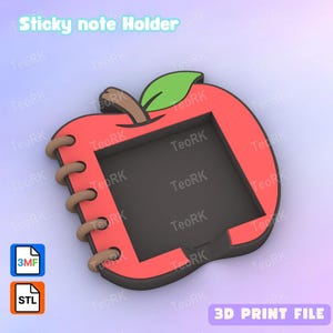 Puede incluir: Un soporte para notas adhesivas con forma de manzana roja con una hoja verde y un tallo marrón. El soporte tiene un interior negro y una encuadernación en espiral en el lateral. El texto "Sticky note Holder" está en la parte superior.
