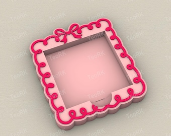 May include: A pink square box with a decorative scalloped edge and a bow on top. The box has a darker pink trim and a square opening in the center. The box is designed with a decorative, feminine aesthetic.