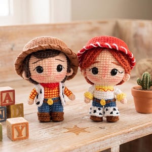 May include: Two crochet dolls featuring characters with large black eyes and rosy cheeks. The left doll wears a brown hat, red scarf, and cow-print vest. The right doll has red hair, a red hat with white trim, and a yellow shirt with cow-print pants.