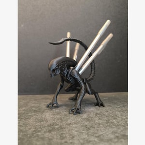 May include: A black Alien figure with a detailed design, featuring a long tail and silver accents. The creature is in a crouching position, showcasing its menacing posture. This collectible item is a unique piece for fans of science fiction.