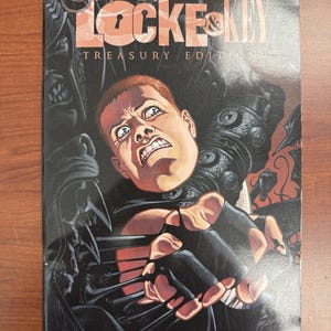 Puede incluir: Portada del cómic "Locke & Key: Crown of Shadows Treasury Edition" de Joe Hill y Gabriel Rodriguez. Presenta un rostro angustiado e imágenes góticas oscuras con el título destacado.