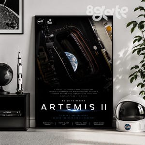 May include: A framed Artemis II poster featuring a view of Earth from space, with the text "WE GO TO RETURN ARTEMIS II." The poster includes the NASA logo and details about the mission, including the names of the crew members.