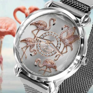 Könnte beinhalten: Silberne Armbanduhr mit hellgrauem Zifferblatt mit vier Flamingofiguren mit Kristallakzenten. Die Uhr hat ein silbernes Mesh-Armband und der Markenname "Jessica" ist auf dem Zifferblatt sichtbar.