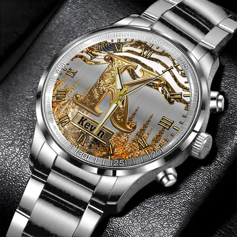 May include: Silver wristwatch with a detailed face featuring a gold-colored letter "K" and the name "Kevin". The watch has a silver band and a decorative background with gold and white accents. Roman numerals mark the hours.