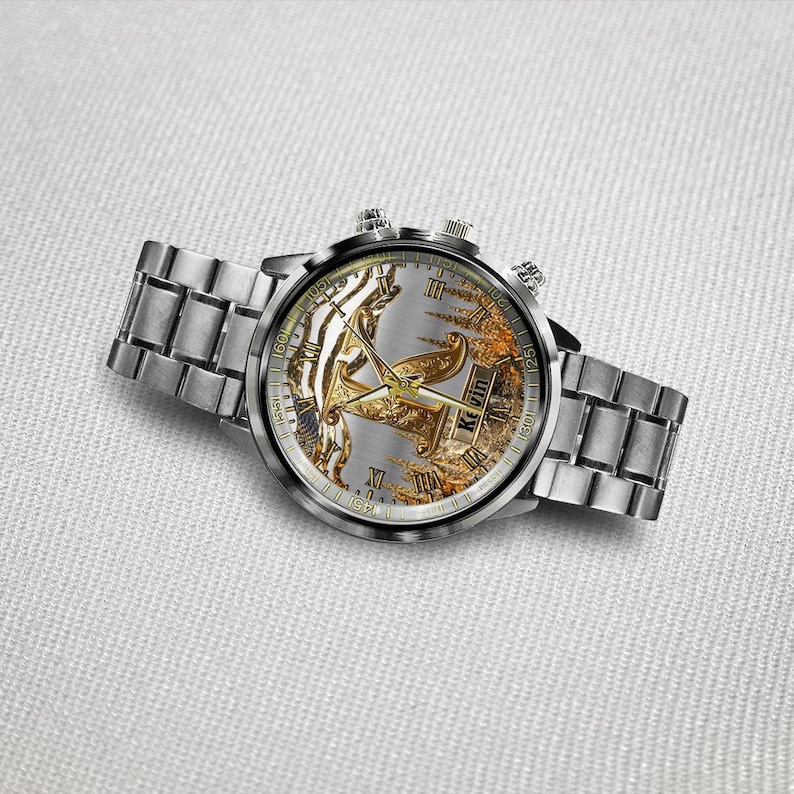 May include: A silver wristwatch with a detailed face featuring gold accents and Roman numerals. The watch has a silver band and two small dials on the side. The watch face has the name "Kevin" on it.