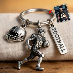 May include: Silver-toned football keychain with a helmet charm, a player figurine wearing a jersey with the number 19, and a tag that says "FOOTBALL". The player figurine is holding a football.