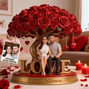 May include: A decorative sculpture of a couple seated under a tree of red roses. The base features the word "LOVE" in gold, with space for custom names. Includes a photo frame and hanging heart ornaments.
