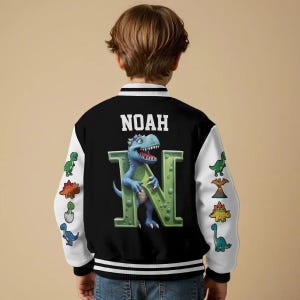 May include: Black and white letterman jacket with the name "NOAH" in white block letters. A blue dinosaur is holding a green "N". The jacket has white sleeves with dinosaur graphics.