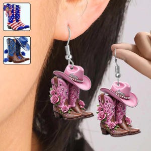 May include: Cowboy boot earrings with a pink cowboy hat. The earrings feature brown boots with pink roses and a pink hat with the name "Anna". The earrings are hanging from silver hooks. Additional images of cowboy boots are in the upper left corner.