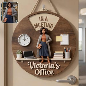 Könnte beinhalten: Ein rundes Türschild aus Holz mit der Aufschrift IN A MEETING und Victoria's Office. Es enthält eine Uhr, eine Miniaturfigur einer Person in Blazer und Rock, einen Laptop, einen Notizblock, Bücherstapel, eine Topfpflanze und einen Stiftehalter.