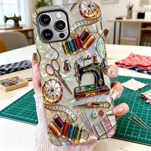 May include: A phone case with a pearlescent finish, decorated with sewing-related items. The design includes a miniature sewing machine, spools of colourful thread, scissors, a thimble, and a measuring tape. The name "Sophia" is also displayed.