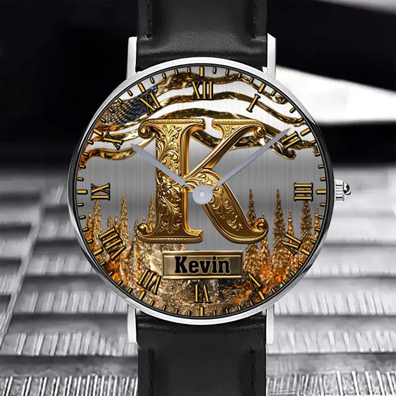 May include: A round wristwatch with a black leather band. The watch face features a gold-colored letter "K" with an ornate design, Roman numerals, and the name "Kevin" in a rectangular box. The background has a gold and silver color scheme.