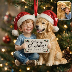 May include: A ceramic Christmas ornament featuring a smiling child in a blue shirt and jeans sitting next to a golden retriever. Both wear red Santa hats and hold a sign that reads Merry Christmas! From Jackie & Coco, suspended by a red ribbon.