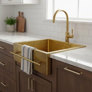 May include: A hammered brass kitchen sink with a matching tap. The sink is rectangular and has a towel rail. A striped towel hangs on the rail. The sink is on a white countertop above dark brown cabinets.