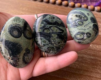 May include: Three green and black polished stones with a swirling pattern. The stones are smooth and oval shaped.