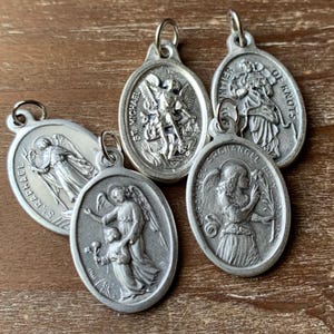 K&ouml;nnte beinhalten: F&uuml;nf silberne, ovale religi&ouml;se Medaillons mit Bildern von Heiligen und Engeln. Die Medaillons haben oben eine Schlaufe zum Aufh&auml;ngen. Die Medaillons zeigen folgenden Text: "St. Michael", "St. Raphael", "Archangel St. Gabriel", "Our Lady of Knots" und "Miraculous Medal".