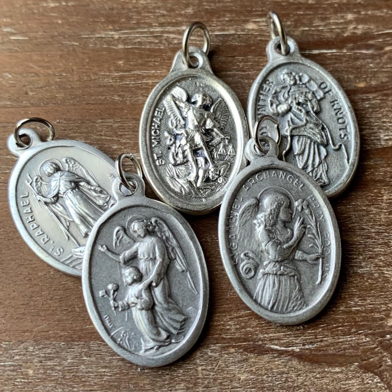 K&ouml;nnte beinhalten: F&uuml;nf silberne, ovale religi&ouml;se Medaillons mit Bildern von Heiligen und Engeln. Die Medaillons haben oben eine Schlaufe zum Aufh&auml;ngen. Die Medaillons zeigen folgenden Text: "St. Michael", "St. Raphael", "Archangel St. Gabriel", "Our Lady of Knots" und "Miraculous Medal".