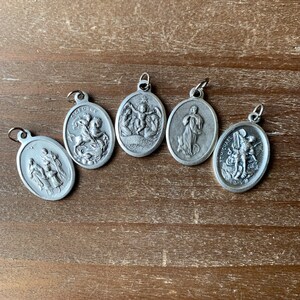 K&ouml;nnte beinhalten: F&uuml;nf silberne ovale Anh&auml;nger mit religi&ouml;sen Bildern. Die Anh&auml;nger zeigen Bilder des Heiligen Georg, der Jungfrau Maria, des Heiligen Michael und zwei weiterer religi&ouml;ser Figuren.
