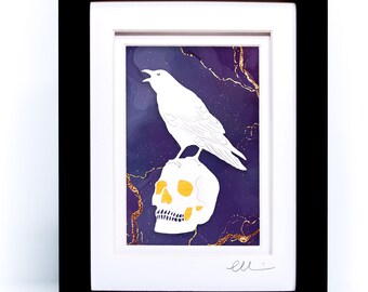May include: A framed art print featuring a white raven perched on a white skull against a deep purple background with gold marble-like veins. The artwork is enclosed in a black frame with a white mat and includes a signature at the bottom right.