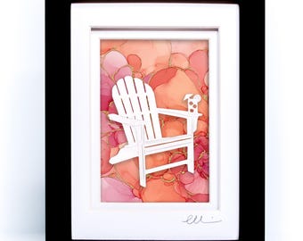 May include: A framed artwork featuring a white Adirondack chair silhouette layered over an abstract background of blended pink, coral, and orange alcohol ink washes with gold accents. The piece is encased in a black frame with a white mat.