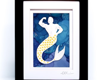 May include: A framed art print featuring a merman with a muscular upper body and a yellow-scaled tail, set against a blue alcohol ink background with abstract circular patterns. The artwork is enclosed in a black frame with a white mat board.