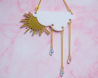 May include: A gold necklace with a white cloud pendant and a sun charm. The necklace has three dangling crystal drops.