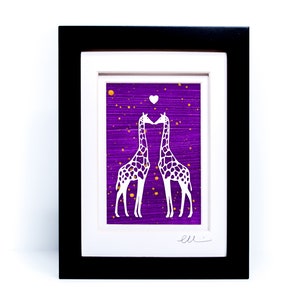 May include: Framed paper cut art featuring two white giraffes kissing on a purple background with gold glitter. The giraffes are silhouetted against the purple background and have a small white heart above them. The artwork is signed "ell"