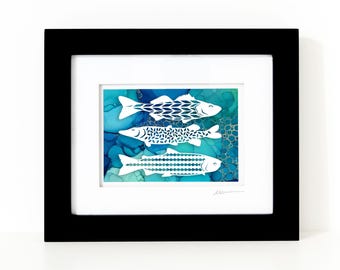 May include: A framed artwork featuring three white fish silhouettes layered over a vibrant blue and teal alcohol ink background. The fish are decorated with distinct geometric patterns and are enclosed in a simple black frame with a white mat.