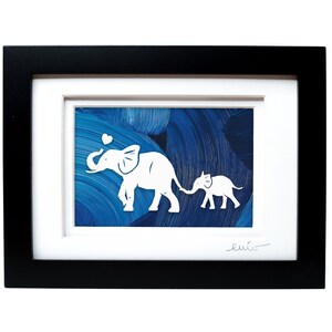 May include: A framed artwork featuring a white paper cutout of an adult elephant and a baby elephant holding tails, with a small heart above the adult. The background is a textured deep blue painted surface, enclosed in a black rectangular frame.