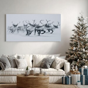 May include: A monochrome print of reindeer in motion adorns the wall above a cream sofa. A decorated Christmas tree with fairy lights and presents is to the right. A round wooden coffee table sits on a jute rug, creating a festive living room scene.