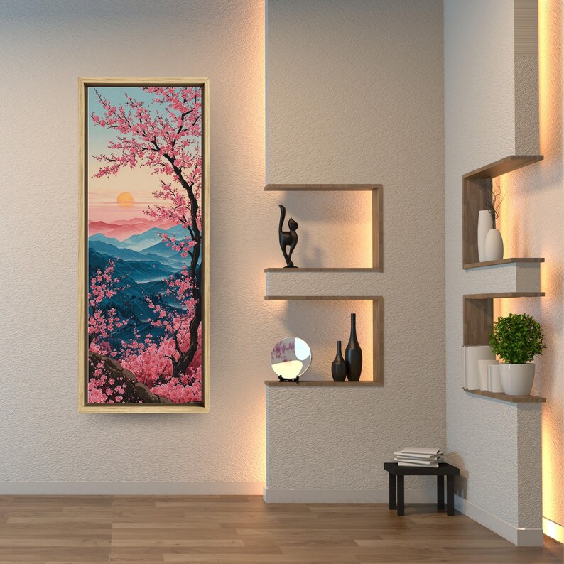 May include: A framed landscape painting shows a cherry blossom tree with pink flowers against blue mountains and a setting sun. The artwork is displayed on a textured white wall in a modern interior setting.