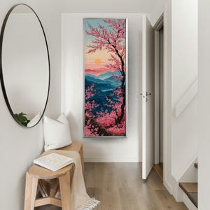 May include: A framed vertical art print showing a cherry blossom tree in full bloom against a backdrop of blue mountains and a sunset. The artwork uses pink and red tones to depict the sky and blossoms.