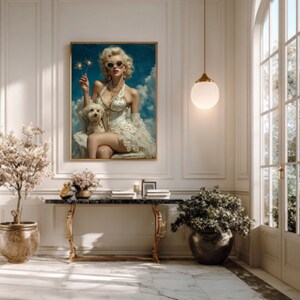 以下が含まれることがあります： 金髪とサングラスの女性が手持ち花火を持ち、小さな白い犬と一緒の額装されたアートワーク。女性は白いドレスと真珠のネックレスを着用しています。背景は雲のある青い空です。アートワークは、大理石の床と装飾的なテーブルのある部屋に飾られています。