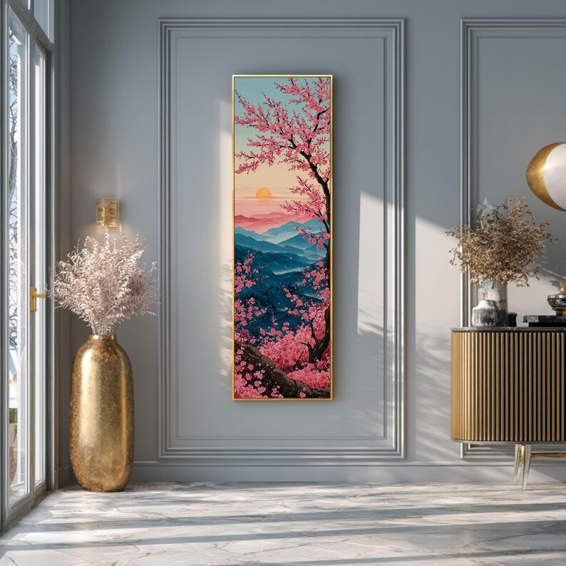 May include: Vertical framed artwork showing a tranquil landscape. A cherry blossom tree with pink flowers is on the right, with a sunset and mountains in the background. The artwork is framed in gold and hangs on a grey wall.