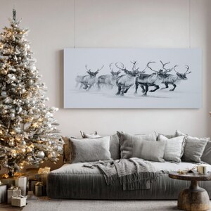 May include: A monochrome painting of reindeer running in snow is displayed above a grey sofa with cushions and a throw. A decorated Christmas tree stands to the left, with presents beneath it. The room has a neutral colour palette.